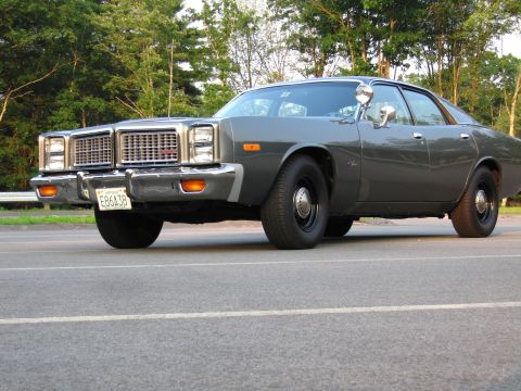 1991 Ford LTD Crown Victoria - Low front three-quarter view of a dark grey late-1970s Dodge Monaco-style full-size four-door sedan on black steel wheels, with stacked qua…