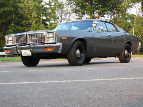 1991 Ford LTD Crown Victoria - A dark gray 1970s Dodge four-door sedan photographed from a low front three-quarter angle, showing a chrome grille, dual round headlights,…