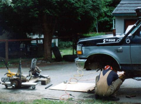1995 Ford F-150 - Mechanic works on the front axle of a 1995 Ford F-150 truck, which has been lifted for service.