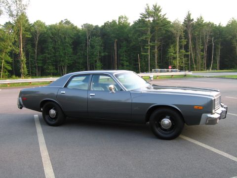 1991 Ford LTD Crown Victoria - A gray 1977 Dodge Monaco sedan is parked in a lot with trees in the background.