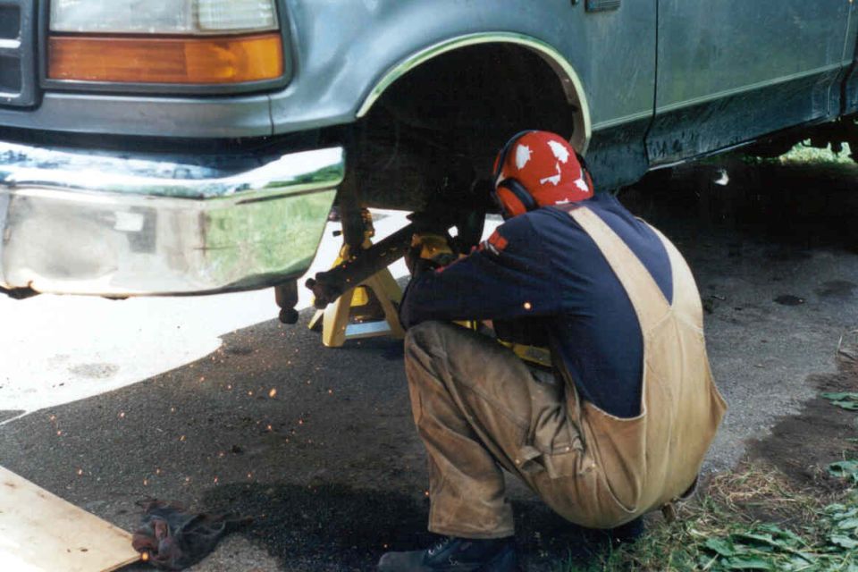 1995 Ford F-150 front suspension work, person in overalls and helmet crouched down