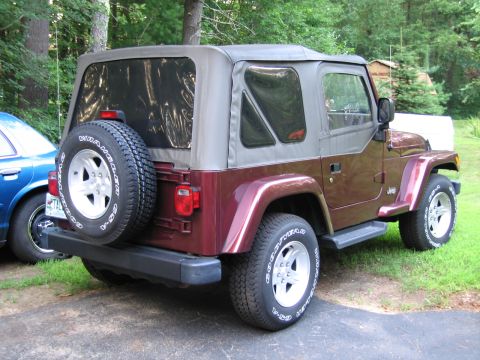 1991 Ford LTD Crown Victoria - Rear view of a maroon Jeep Wrangler, showing its soft top and spare tire mounted on the tailgate. Another vehicle is visible to the left.