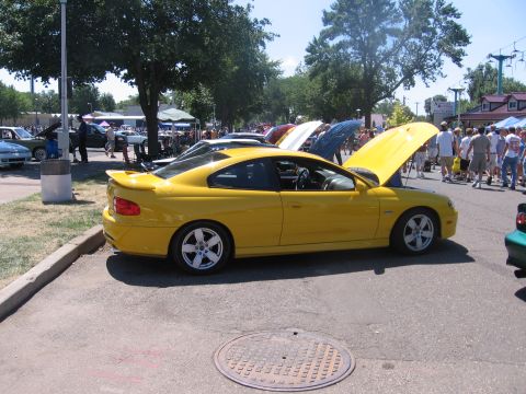 1989 Ford Mustang - A yellow coupe is displayed with its hood open at an outdoor car show.