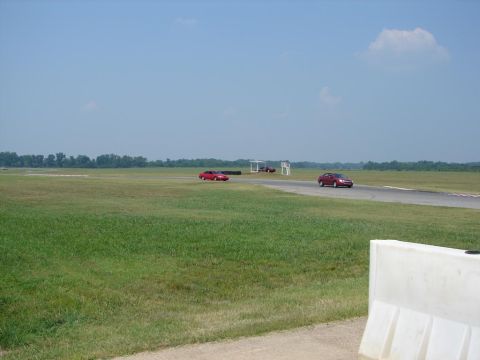 1992 Ford Taurus - Two red sedans are on a racetrack under a clear blue sky with a few clouds.