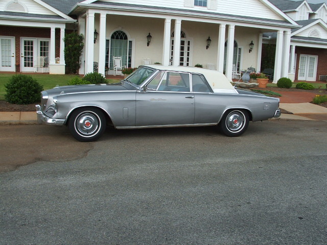 Silver 1961 Studebaker Hawk convertible parked on asphalt in front of a large house with white columns