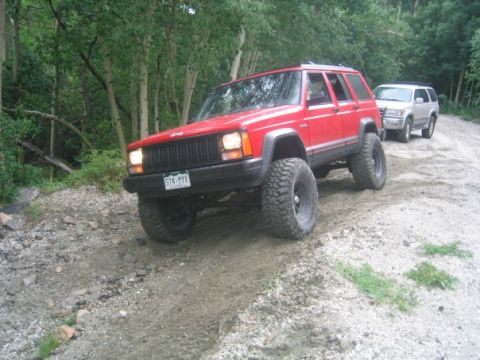 1996 Jeep Cherokee - A red 1996 Jeep Cherokee navigates a dirt road in a forest, with another SUV following behind.