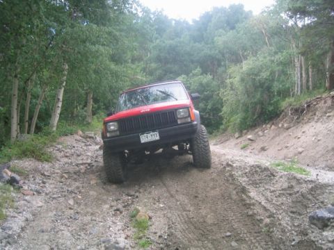 1996 Jeep Cherokee - Red Jeep Cherokee navigating a rough, off-road trail in a forest.
