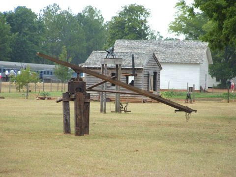 1966 Ford Ranchero - A rustic wooden crane stands in a field, with historical buildings and a train visible in the distance.