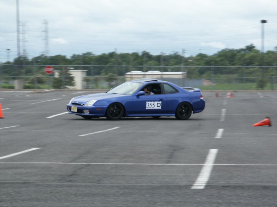 Blue coupe with racing number 355 D on the door driving on a paved course with orange cones