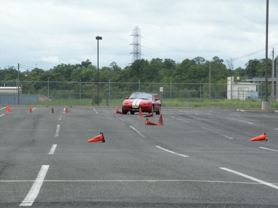 Red sports car with white stripes on hood and trunk, parked in a lot with orange cones