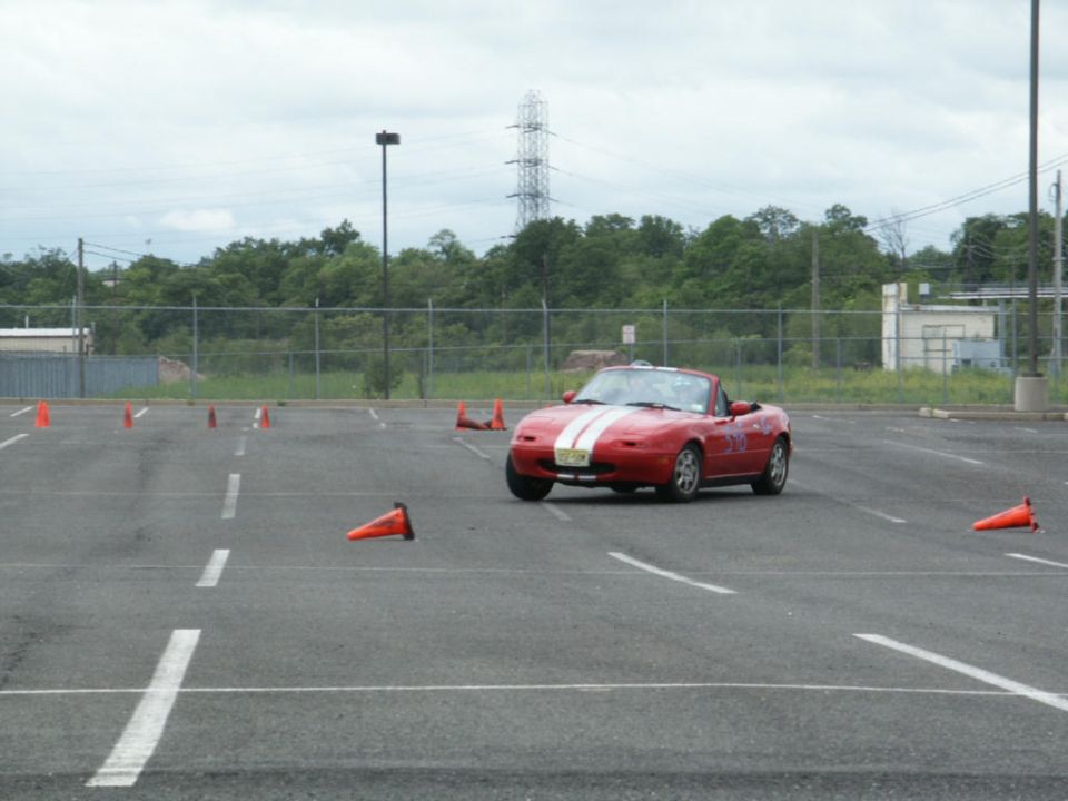 Red convertible sports car with white stripes navigating a cone course in a parking lot