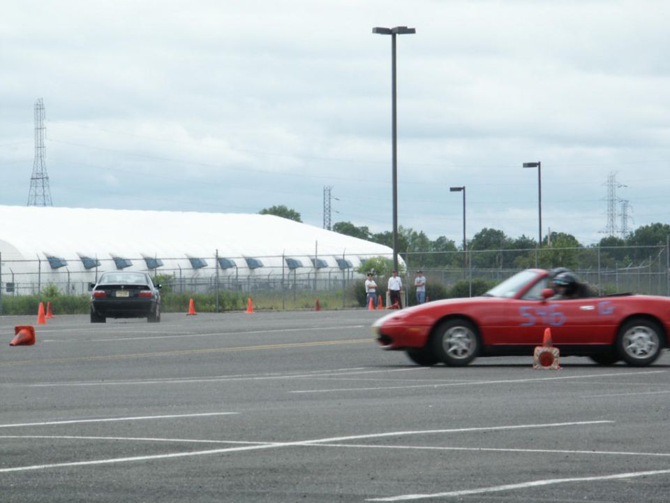 Red convertible sports car with number 546 on door, driving on asphalt track past orange cones