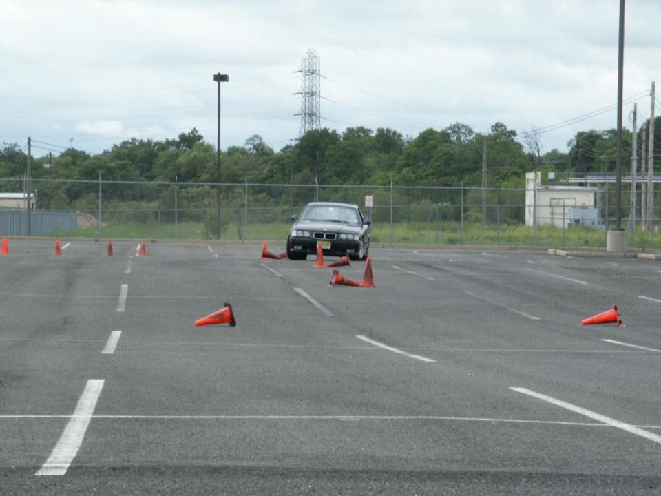 BMW E36 sedan navigating a cone course in a parking lot