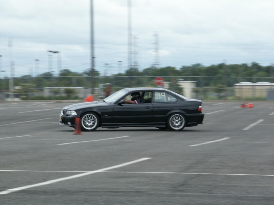 Black BMW E36 coupe on a track, driver visible inside