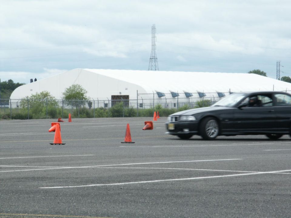 Black coupe navigates a course marked by orange cones in front of a large white building