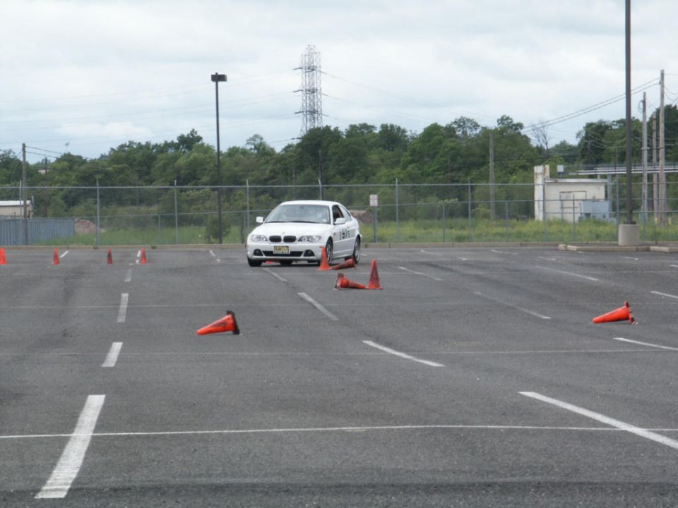 White BMW 3 Series sedan driving through an autocross course marked by orange cones