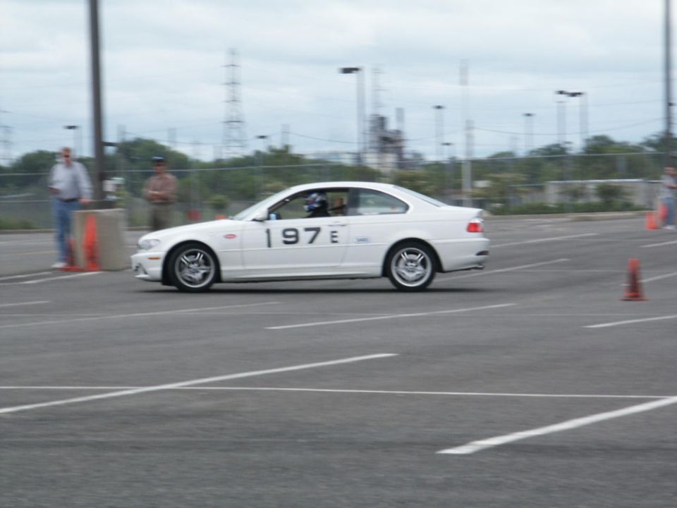 White coupe with '197 E' on the door driving on a paved track with orange cones