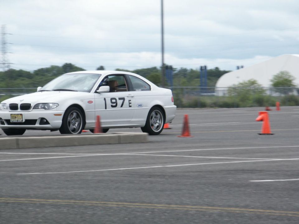 White BMW 3 Series Coupe with racing numbers '197E' on the side, navigating a course marked by orange cones