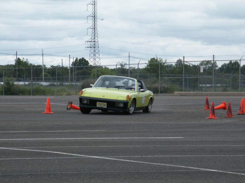 Yellow Porsche 914 driving on a paved course with orange cones
