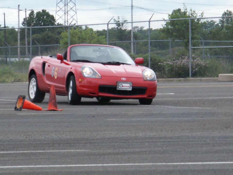 Red convertible sports car with number 66 on the side, driving on asphalt with orange cones