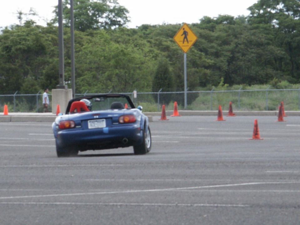 Blue convertible sports car with red interior, seen from the rear on a paved lot with orange cones