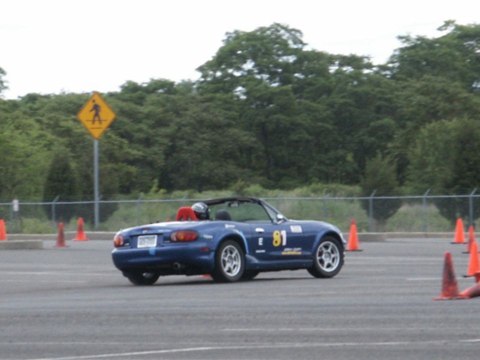 Blue convertible sports car with racing number 81 on the side, driving on a paved course with orange cones