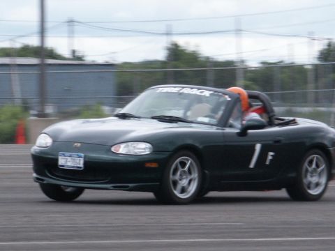 2001 Mercury Grand Marquis - A dark green convertible sports car with racing decals is captured in motion on a paved track.