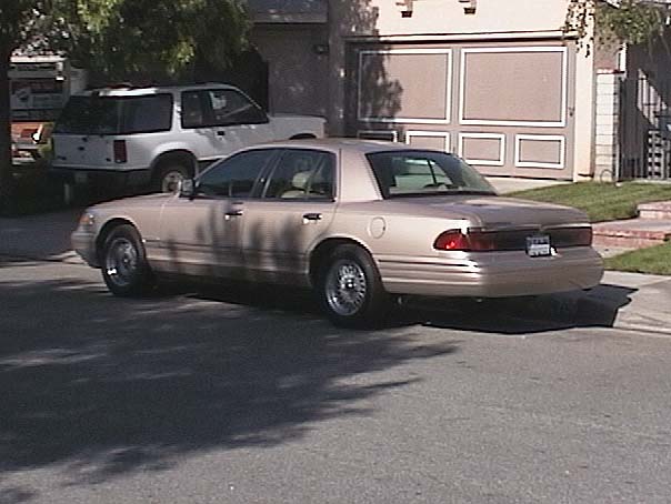 Gold four-door sedan viewed from rear, parked in driveway near white SUV and garage