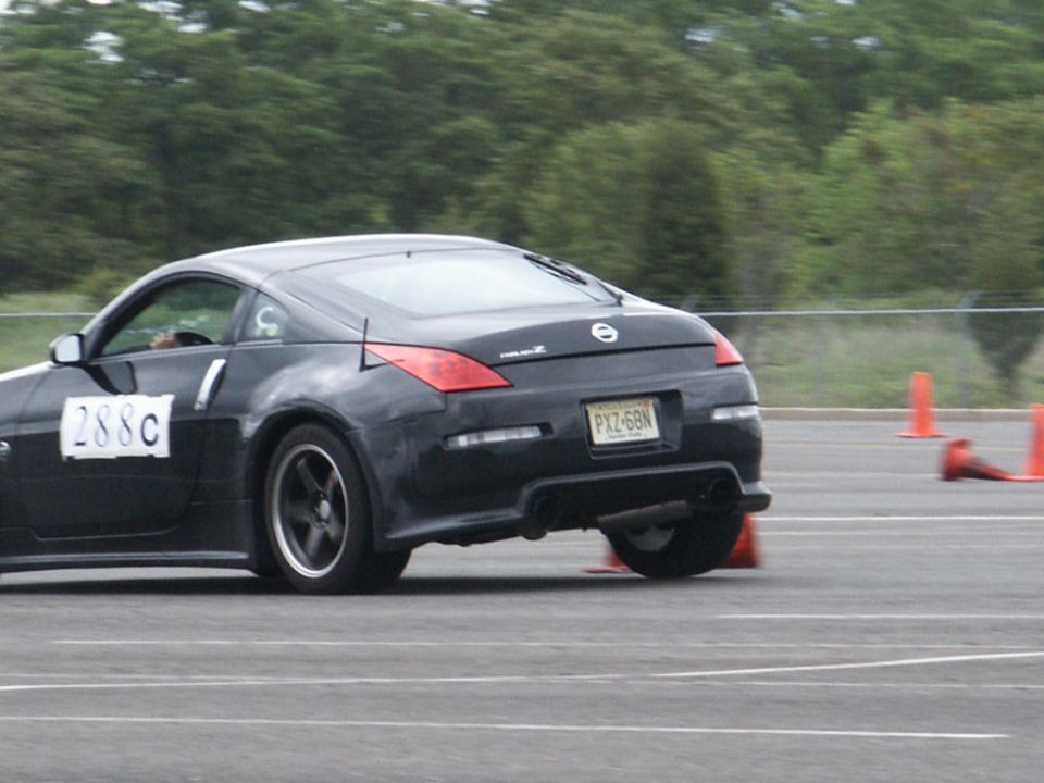 Black Nissan 350Z with racing numbers on door, seen from rear-side angle on a track with orange cones