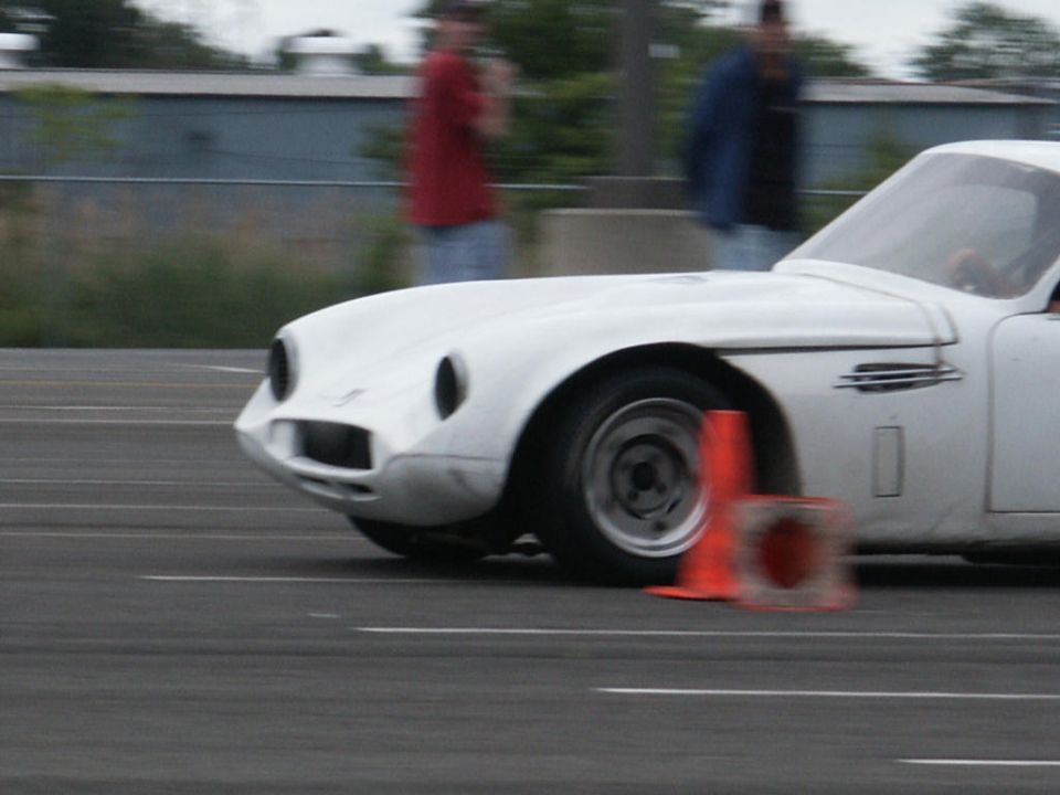 White sports car navigating a course with an orange cone