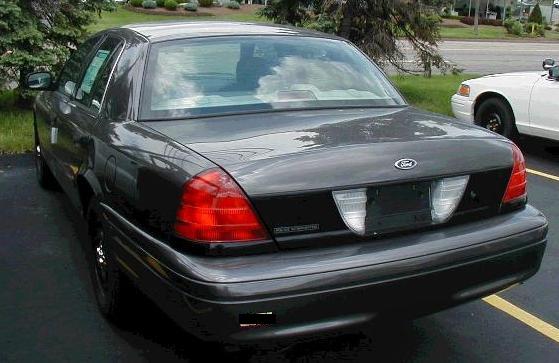 Rear three-quarter view of a black Ford Crown Victoria sedan with black steel wheels in a parking lot