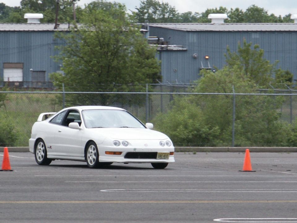 White Acura Integra coupe driving on a paved lot with orange cones