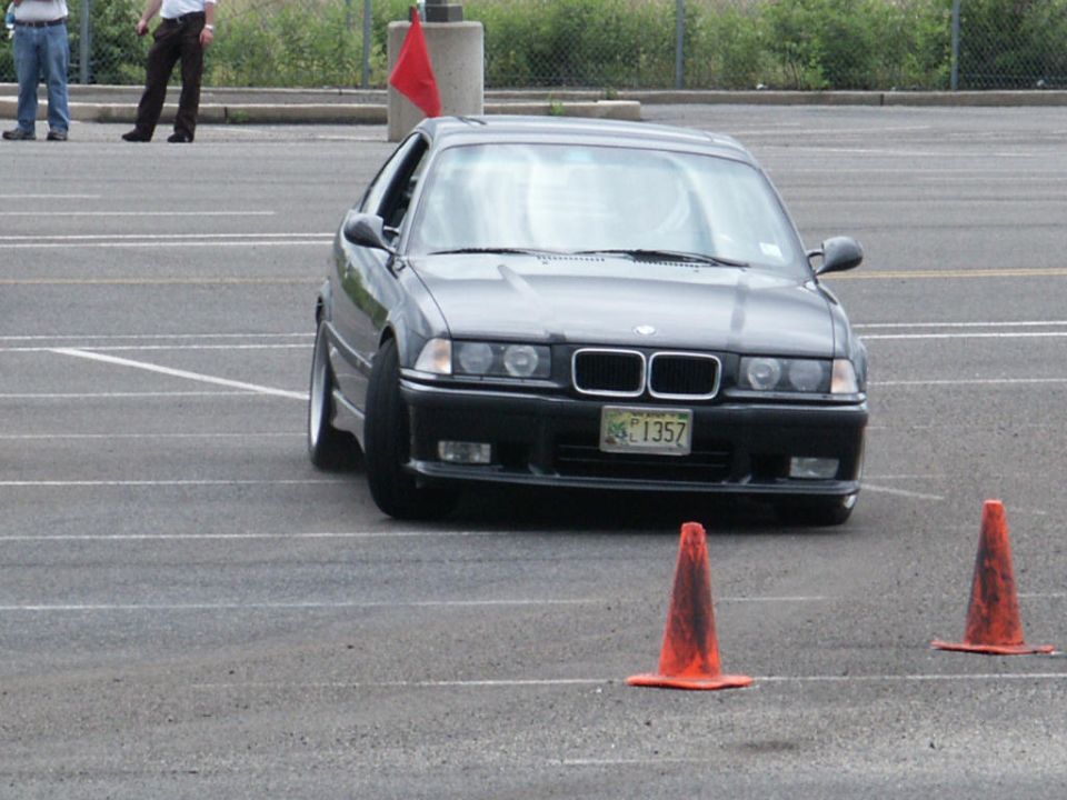 Dark BMW E36 sedan navigating a course marked by orange cones