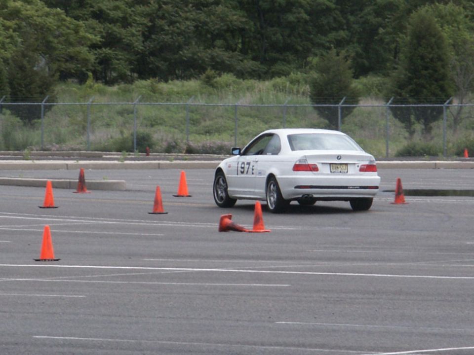 White BMW 3 Series coupe with number 97 on the door, driving on a paved course with orange cones