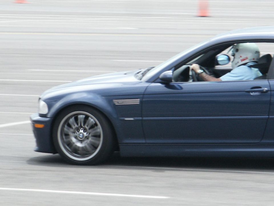 Side view of a blue BMW M3 with a driver wearing a helmet on a track