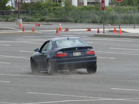 2001 Mercury Grand Marquis - A dark blue BMW coupe is seen from the rear, kicking up dust as it turns in a parking lot marked with cones.