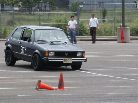2001 Mercury Grand Marquis - A dark gray 1983 Volkswagen Golf GTI navigates a course marked by traffic cones, with two spectators in the background.