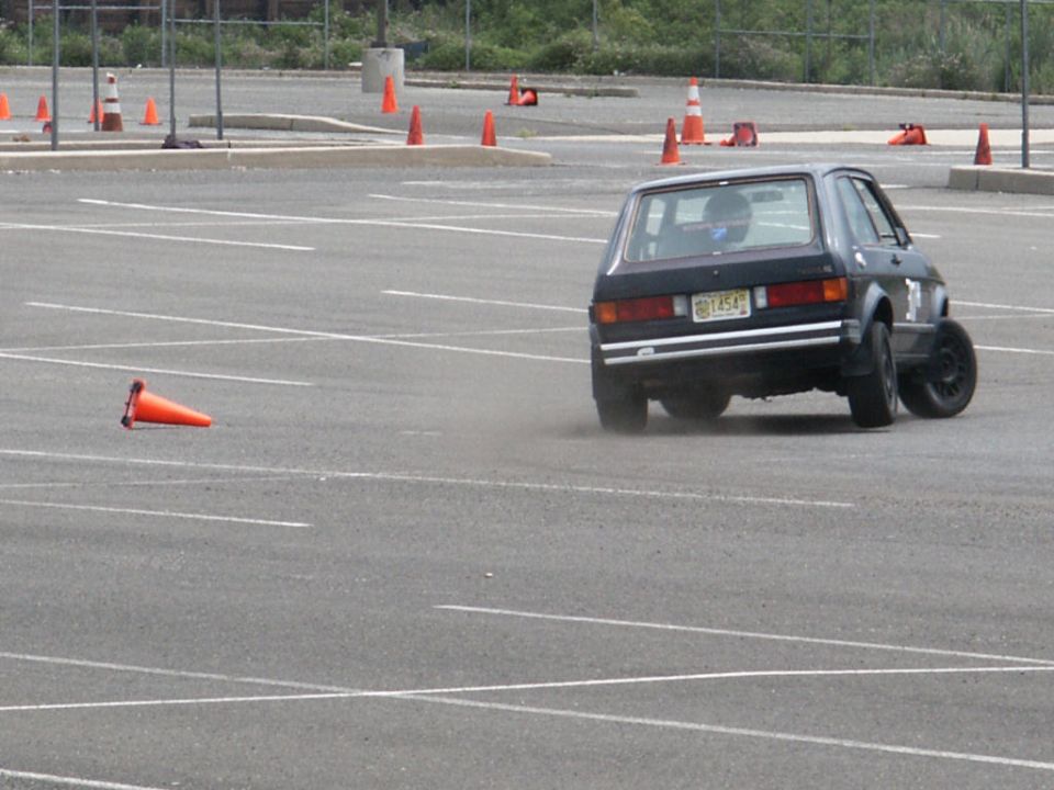 Dark hatchback in a parking lot autocross event, rear view. License plate reads GBT454