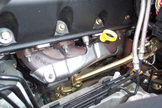 Engine bay close-up of exhaust manifold with stainless heat shield and yellow dipstick
