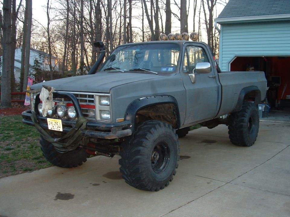Lifted gray Chevy or GMC squarebody 4x4 pickup with mud tires, snorkel and roof lights in a driveway