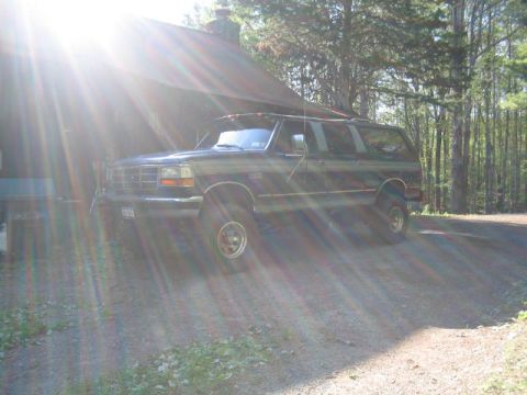 1979 Ford Bronco - This Ford SUV, likely from the early 90s, is parked in a wooded area next to a building.