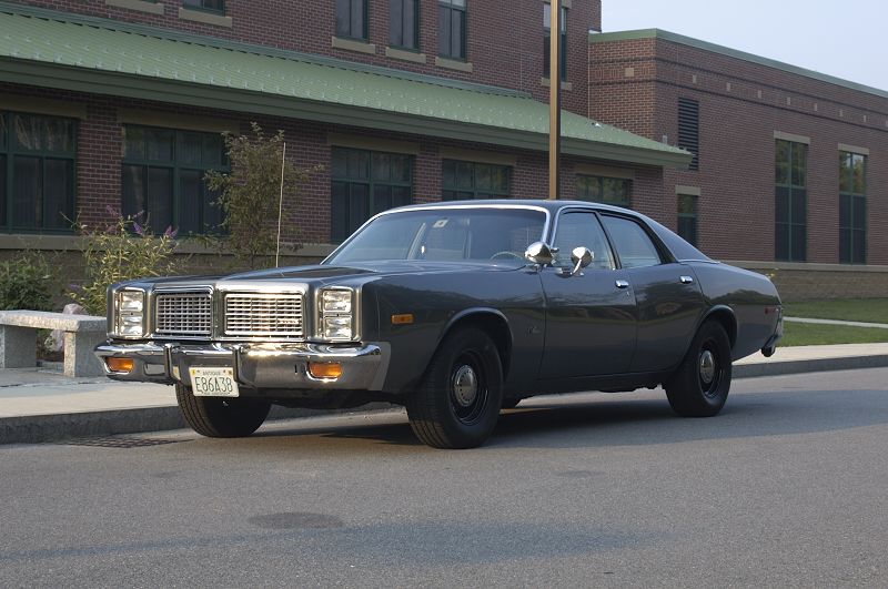 Dark gray 1970s Dodge sedan parked at curb, front three-quarter view.