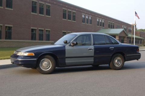 1978 Dodge Monaco - A sedan with two different paint colors on its body is parked in front of a school building.