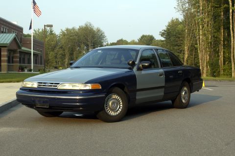 1978 Dodge Monaco - A two-tone Ford Crown Victoria police car is parked in front of a building with trees in the background.