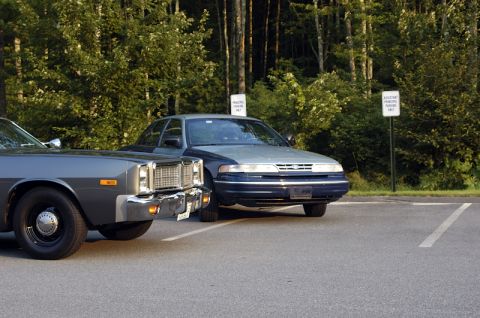 1978 Dodge Monaco - Two cars are parked in a lot, with trees and signs visible behind them.