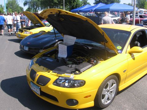 1989 Ford Mustang - A bright yellow Pontiac GTO is displayed with its hood open, revealing the engine and informational notes for onlookers.