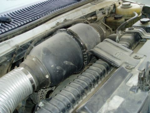 2000 Ford E350 - Engine-bay view of a snorkel-style intake plumbing job: a large black rubber coupler clamped between a flexible silver corrugated duct and…