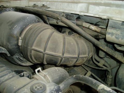 2000 Ford E350 - Engine-bay close-up of a large ribbed black rubber air intake tube running from the air box across the front of the engine, secured with a…