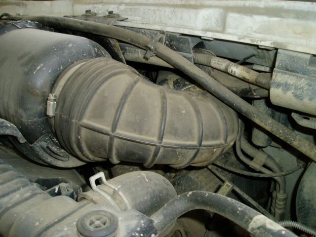 Close-up of a ribbed black air intake tube and clamp in a dusty engine bay