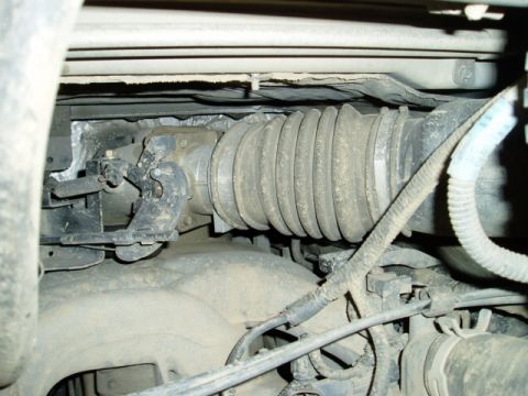 2000 Ford E350 - Dusty under-hood/underbody detail showing a steering shaft with a large accordion-pleated rubber boot running to a U-joint at the steering…